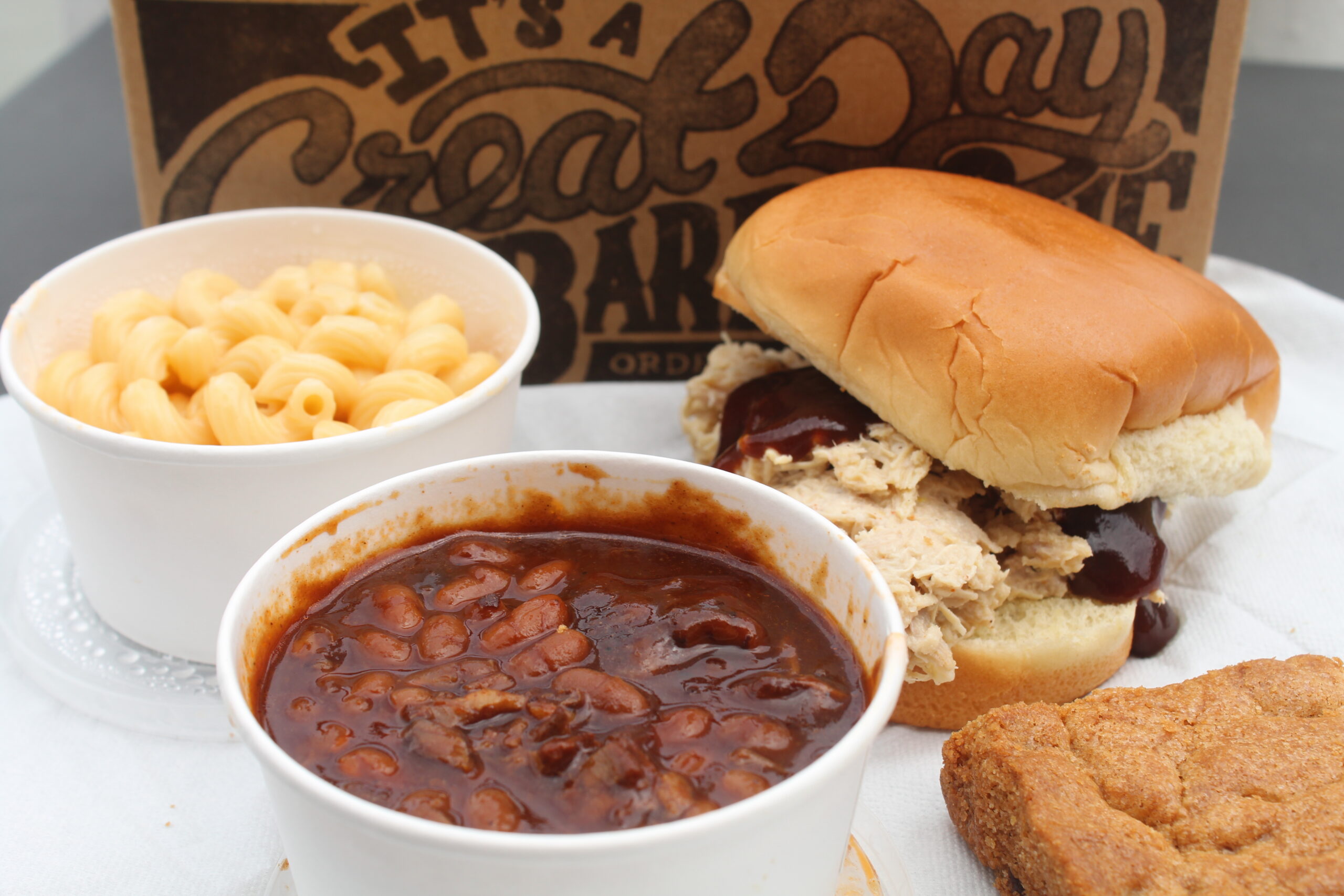 A barbeque sandwich, bowl of macaroni and cheese, bowl of baked beans, and a blondie dessert.